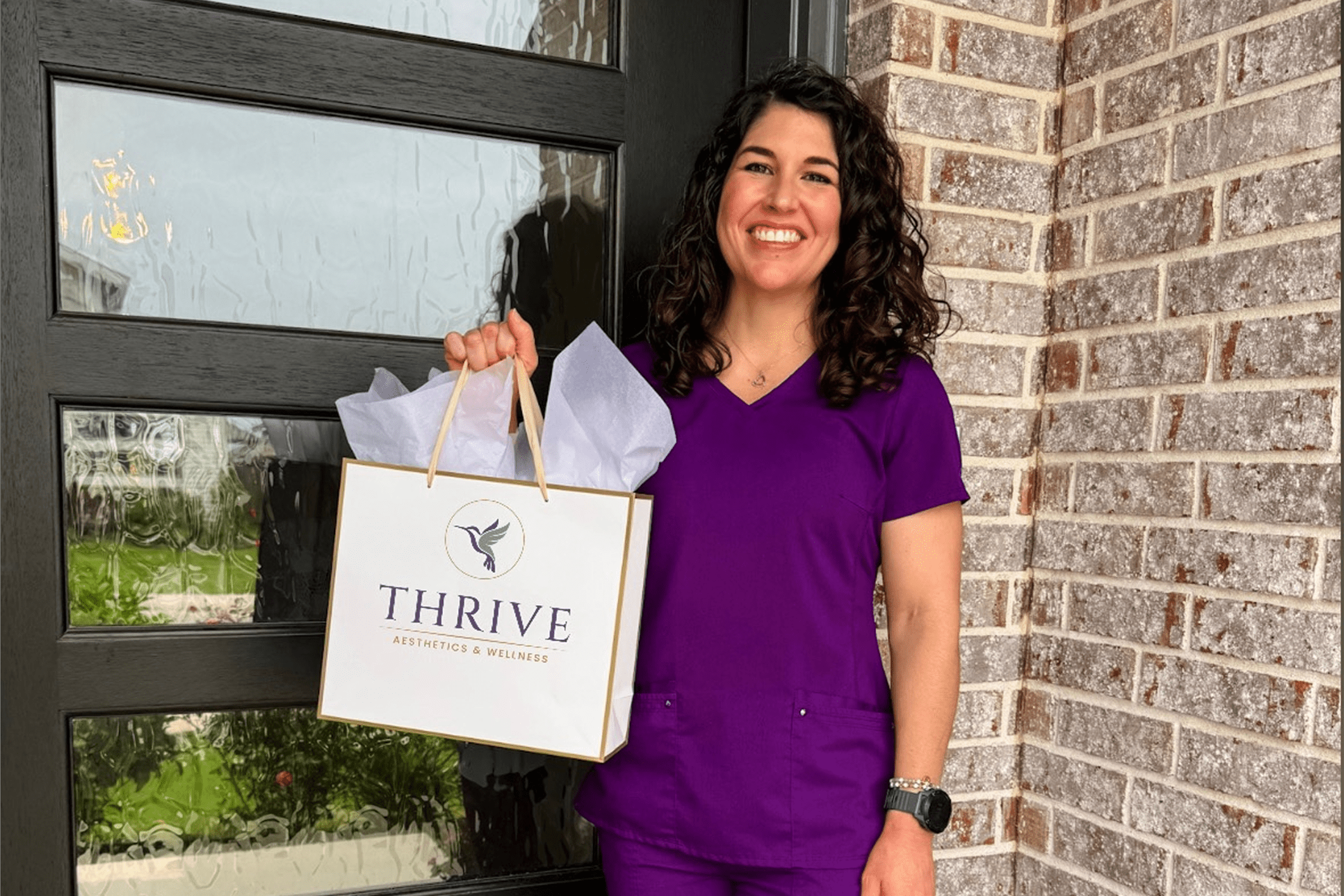 Woman holding Thrive bag, standing outside building.