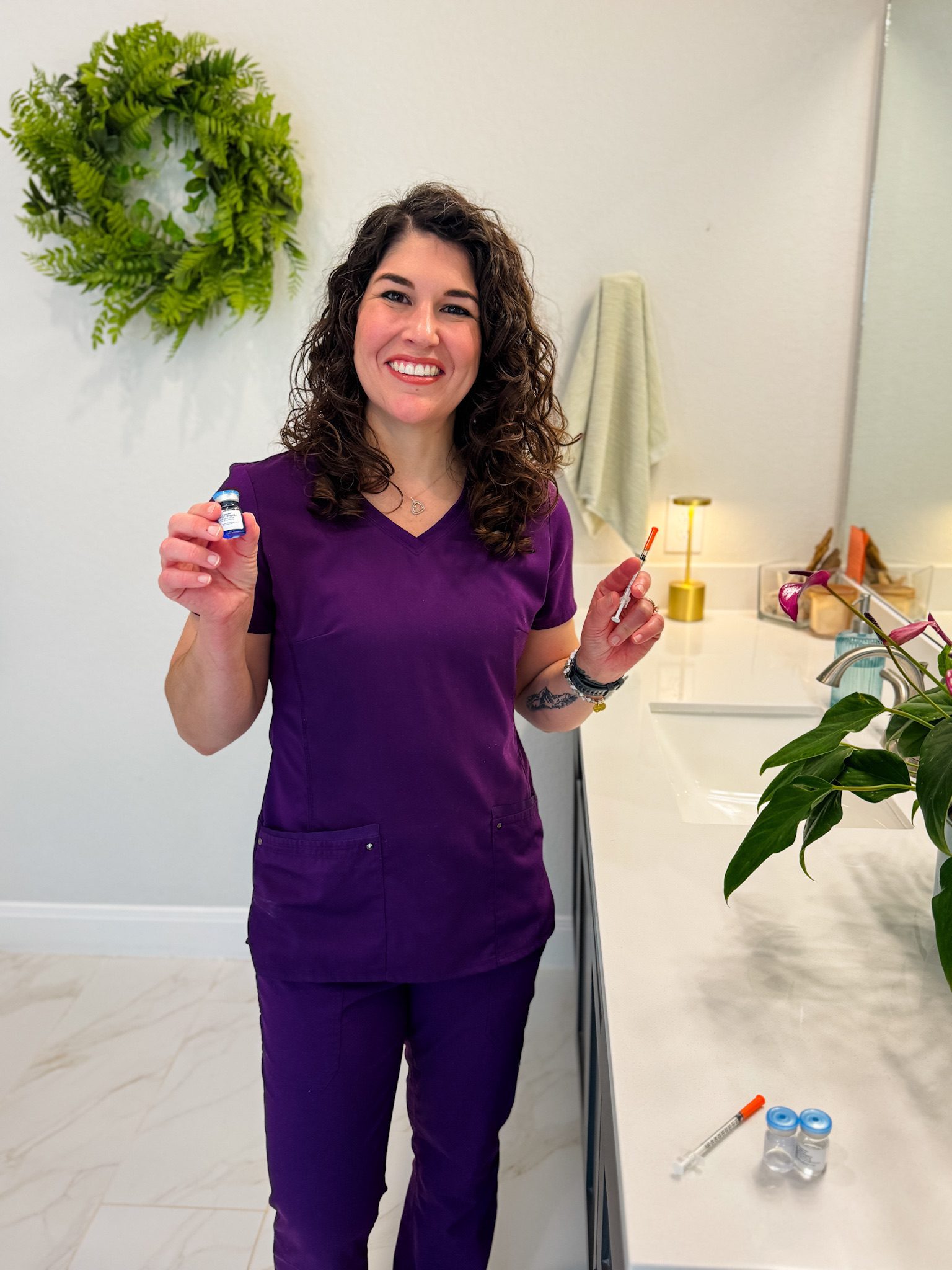 Woman in scrubs holding medical vials, smiling.